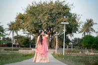 A woman in traditional attire posing gracefully in an outdoor park with trees.
